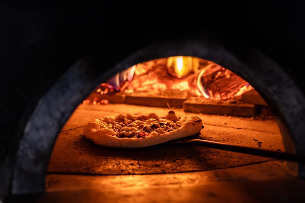 Imagem mostra pizza assada em forno a lenha.